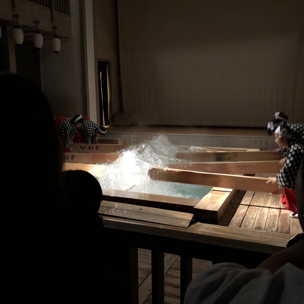 The lights are out in this photo and the women are bent over so they can use the paddles to splash the water out of the pool.