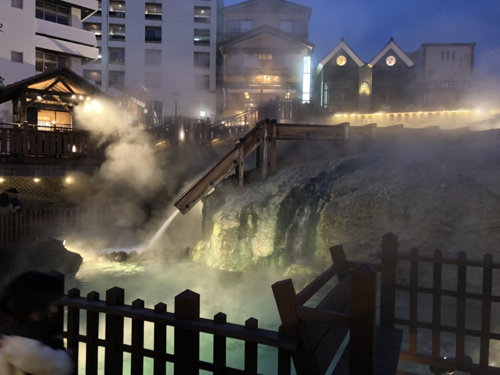 A night view of the lower end of the hot water fields. You can see a wooden chute bringing water down, and the whole thing is wreathed in hot steam.