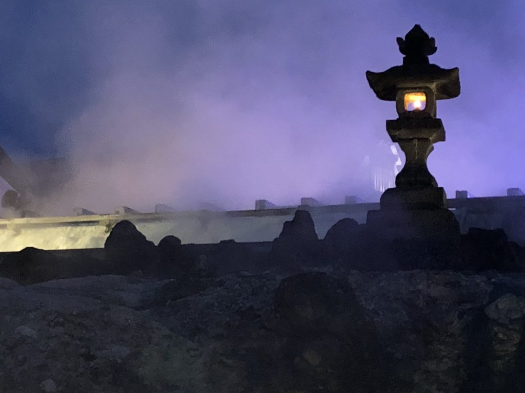 A lit stone lantern at night. Purple steam rises up behind it.