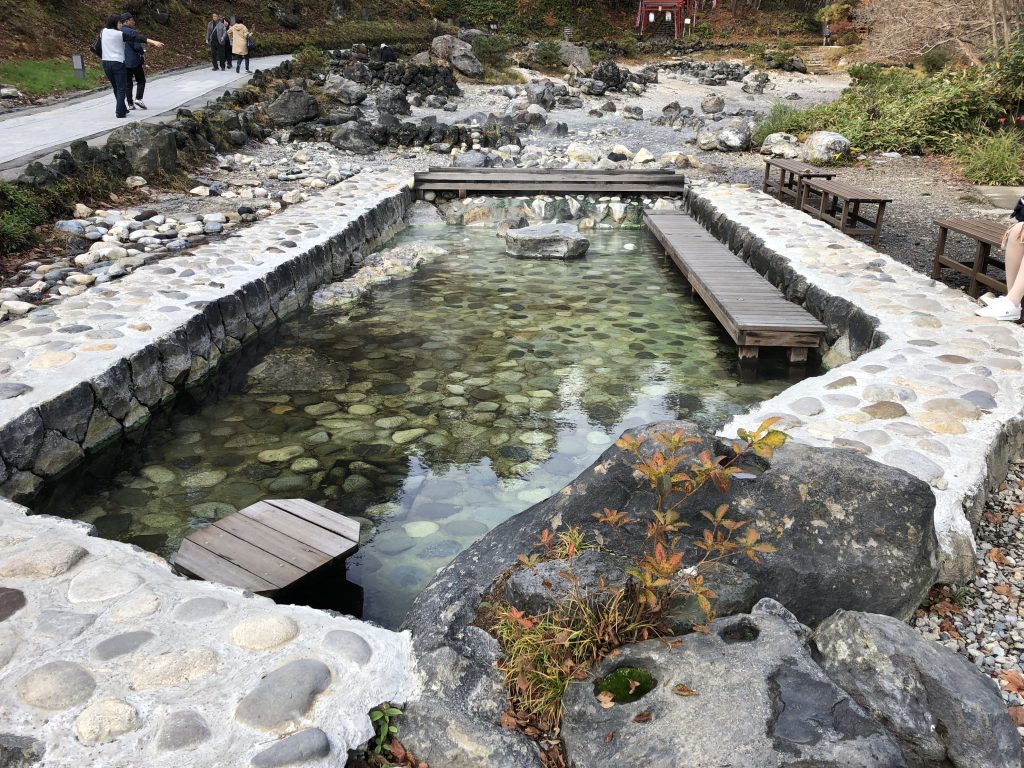 A rectangular stone pool surrounded with wooden benches and greenery.