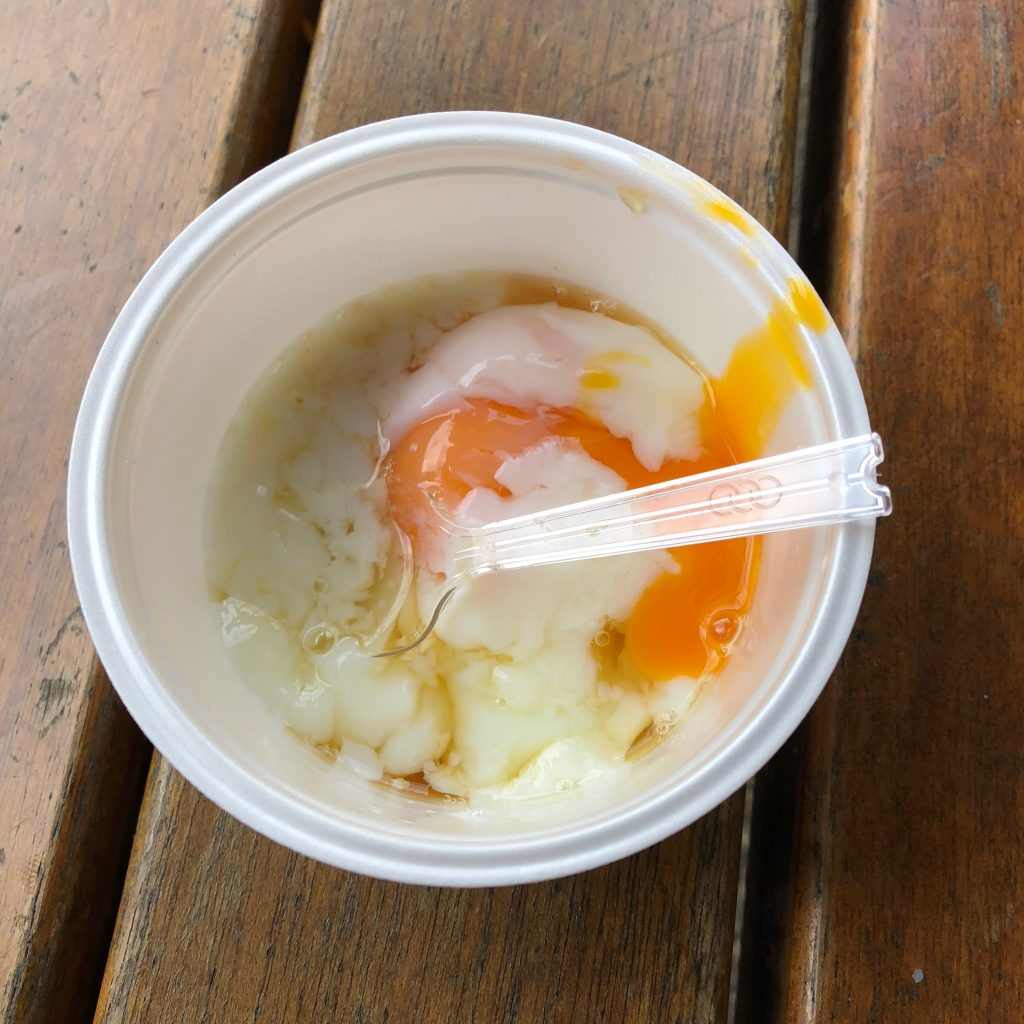 A runny egg in a small styrofoam bowl with brown broth poured over it. It looks a little lumpy in this picture.
