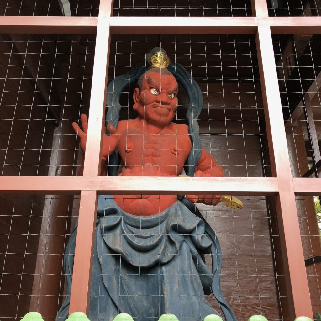 A red statue behind protective lattice. He's muscled and scary and his mouth is closed.