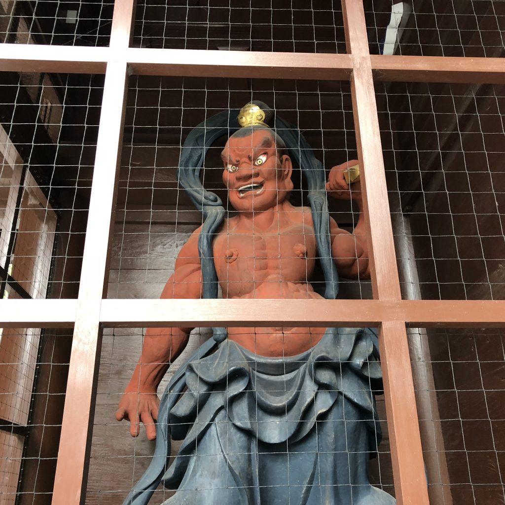 A red statue behind protective lattice. He's muscled and scary and his mouth is open.