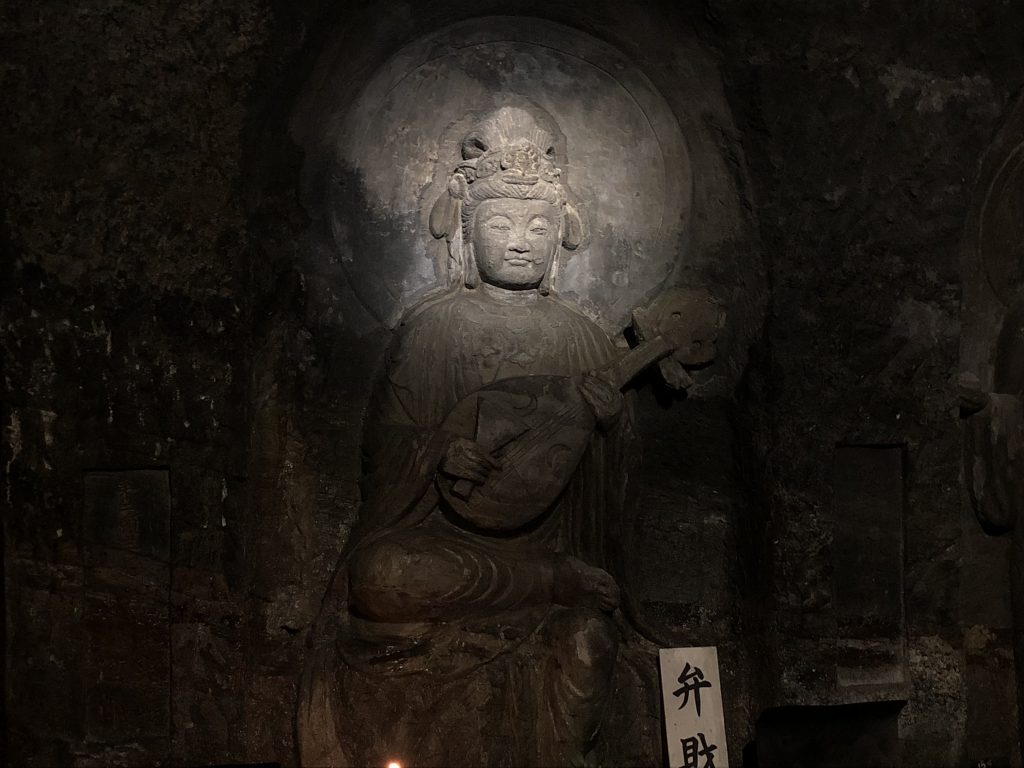 A statue of a woman holding a lute carved into a cave wall.