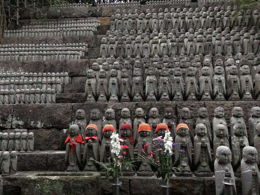 Several outdoor stone shelves of middling to small Jizo statues. At least a hundred are in the picture.