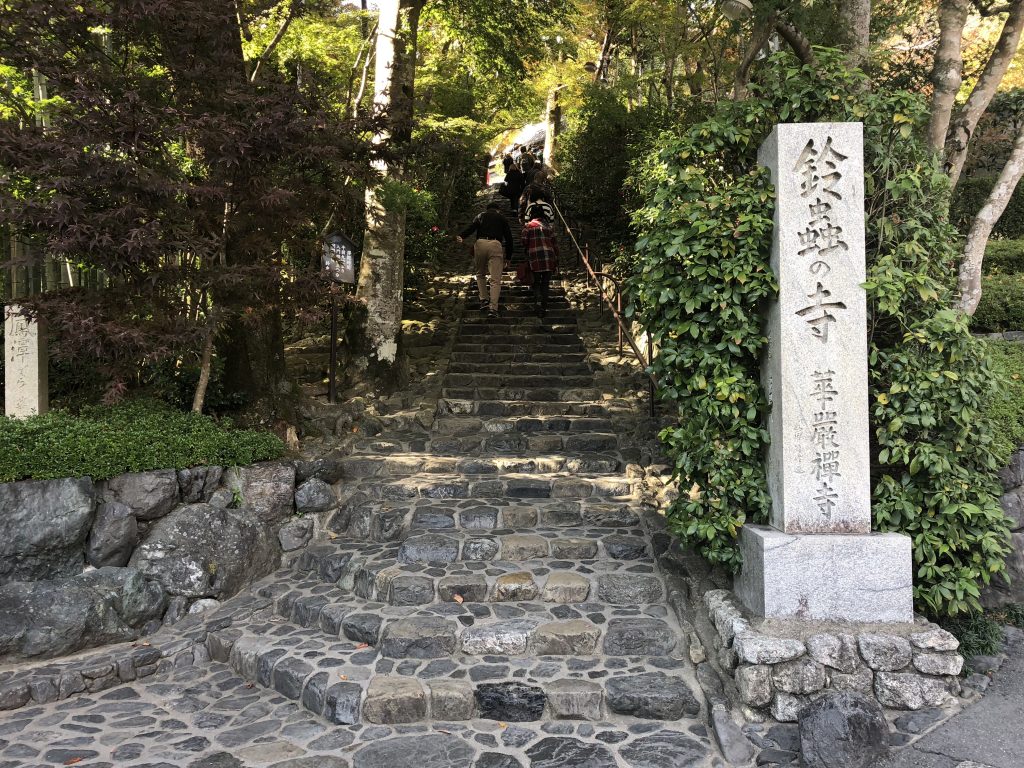 A flight of stone steps going up into the forest. A stone column in the front has the name of the temple on it.