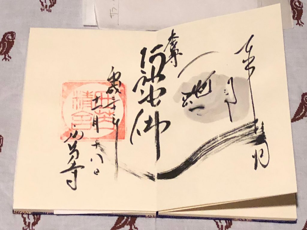 A goshuin spanning two full pages. The calligraphy is very artfully done, and contains an illustration of a severe-looking man.