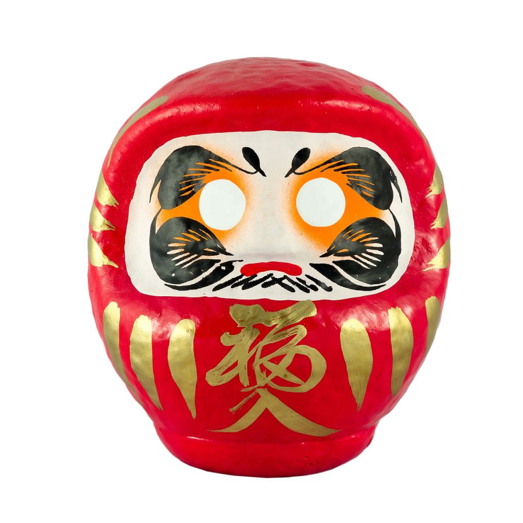 A daruma doll. It is round with a red body and hood, golden accents, and wide white eyes.