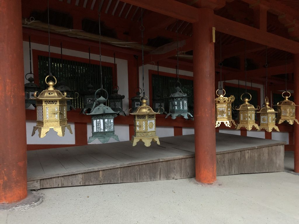 Metal lanterns hanging from the roof of the shrine. They are green and brass.