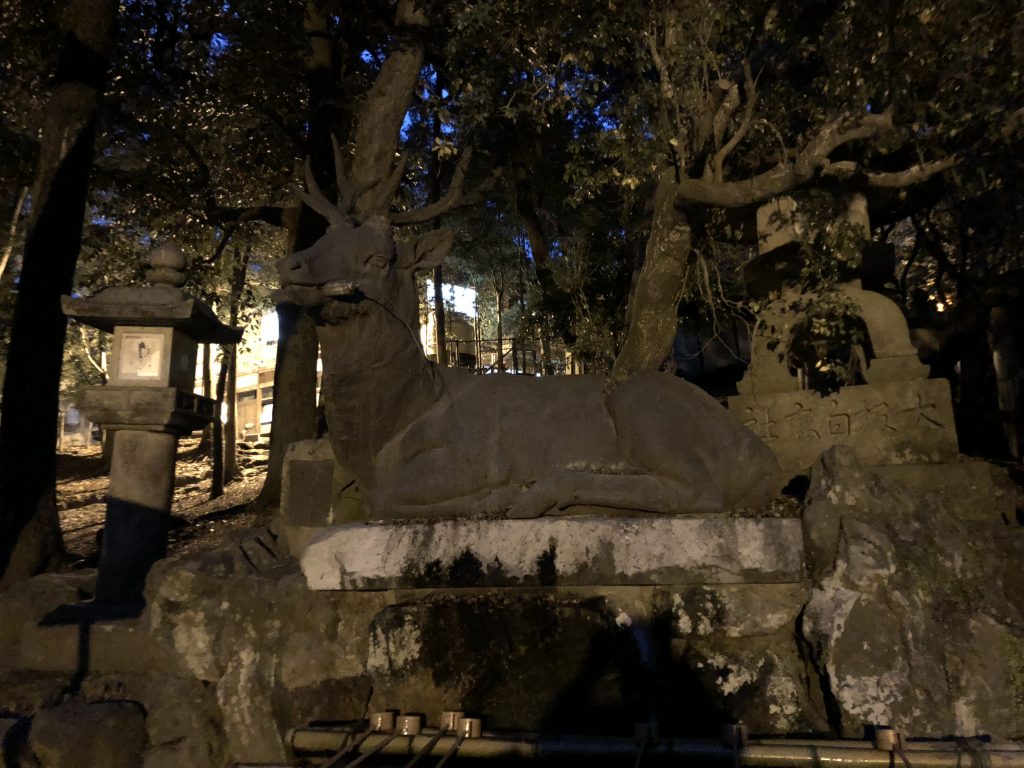 A massive stone deer reclining next to a stone lantern.