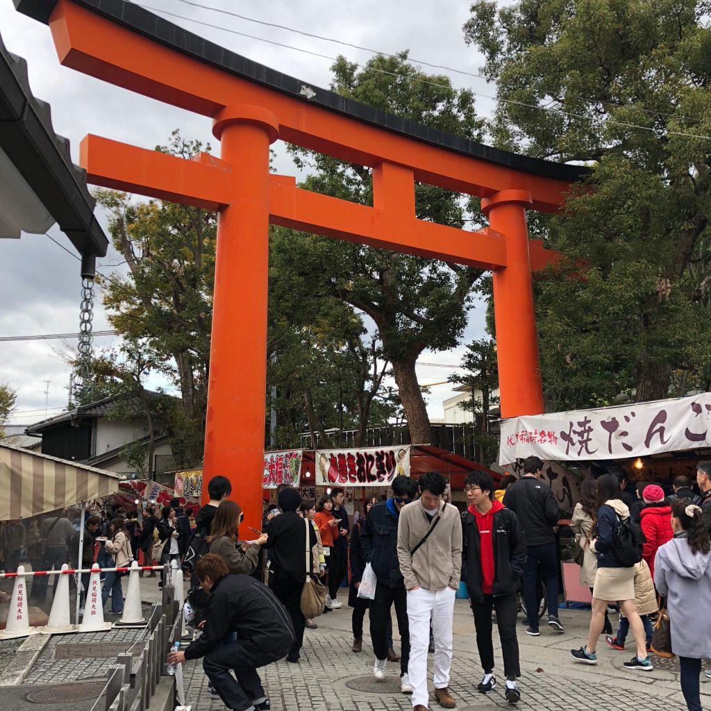 A large torii gate surrounded by food and souvenir stalls.