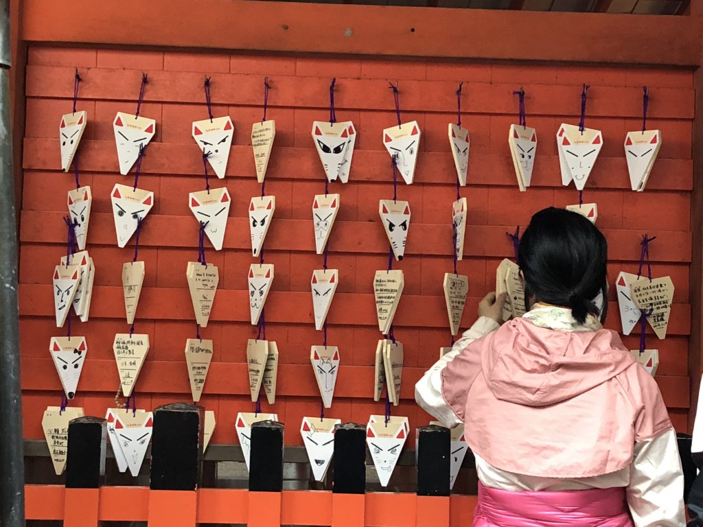 A red wall with lots of little fox-shaped ema hanging from it.