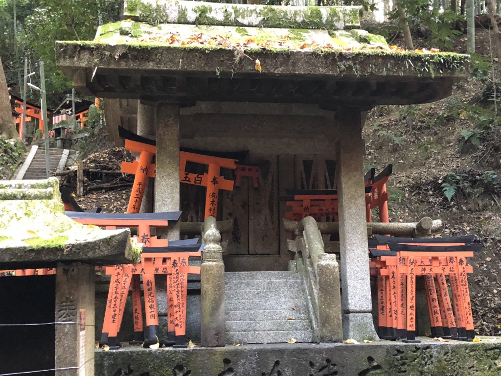 A mossy stone altar full of stacks of tiny torii with wishes written on them.